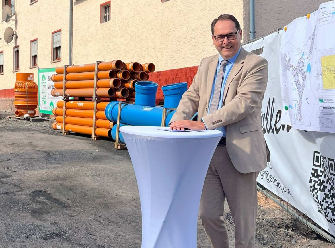 Im Bild sieht man Herrn Hubner, Werkleiter der Wasserwerke Sonneberg. Er trägt einen Anzug und steht an einem Rednerpult. Er lächelt freundlich in die Kamera.